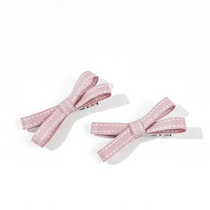 Dettaglio di due fiocchi rosa per capelli con bordi cuciti bianchi e clip in metallo argento