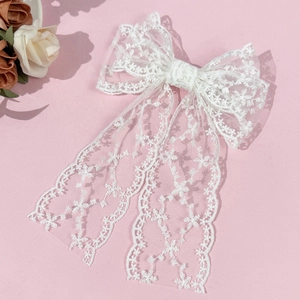 Close-up of white lace bow hair clip with floral embroidery and elegant long ribbon tassels