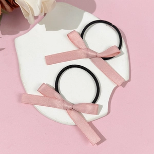 Détail de deux chouchous à nœuds en satin rose sur un support en pierre blanche