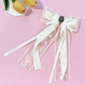 Detailed close-up of a white lace bow hair clip with vintage dark gemstone and bronze relief