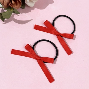 Gros plan sur deux chouchous nœuds en satin rouge avec élastiques noirs sur fond rose