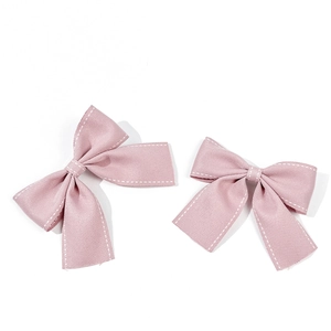 Dettaglio dei fermacelli a fiocco rosa con cuciture bianche su sfondo bianco pulito