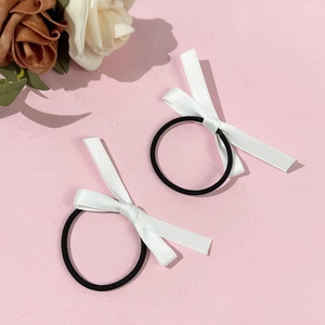 Détail de deux élastiques à cheveux avec nœuds en satin noir et blanc sur fond rose