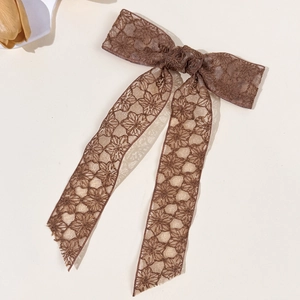 Detail of coffee brown lace bow hair clip with intricate floral embroidery and long ribbons