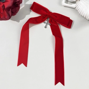 Detail of red velvet bow hair clip with silver vintage cross charm and long streamers