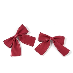 Dettaglio di fiocchi per capelli rosso scuro con cuciture bianche a contrasto su tessuto