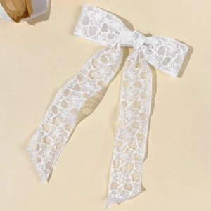 Close-up of a white lace bow hair clip with floral embroidery and long tassels