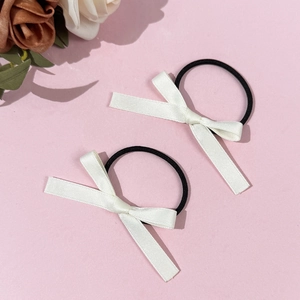 Détail de deux chouchous nœuds en satin crème sur élastiques noirs avec décor de fleurs