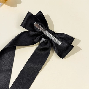 Elegant black satin ribbon bow hair clip with silver metal charm on a beige background