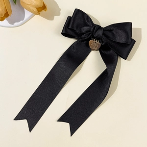 Detail of elegant black satin bow hair clip with engraved golden heart pendant