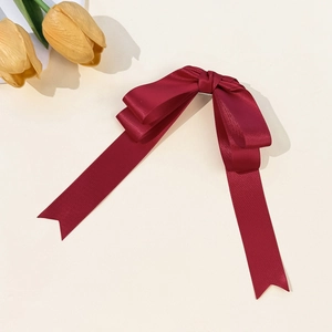Detail of a dark red satin bow hair clip with long ribbons and a silky texture finish