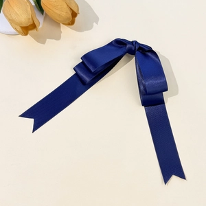 Detailed close-up of dark blue satin bow hair clip with long elegant ribbons on plain surface