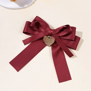 Eleganter weinroter Satin-Doppelbogen-Haarclip mit goldenem Herzanhänger auf beigem Hintergrund