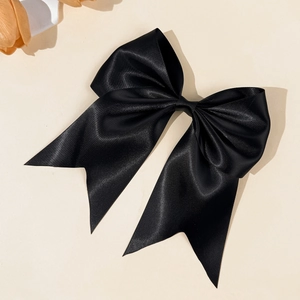 Close-up of a large black satin bow hair clip with elegant silk texture on a beige background