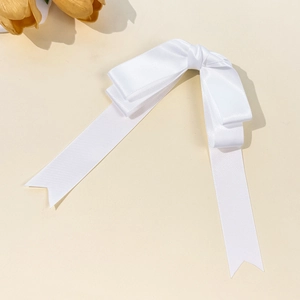 Detail of elegant white satin double bow hair clip with long ribbons on beige background