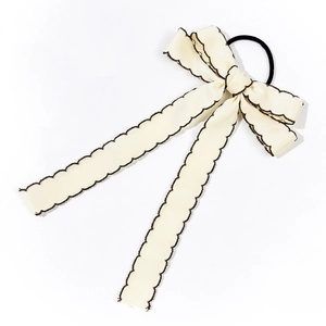 Detailed macro view of cream-colored ribbon hair tie with black scalloped edge texture