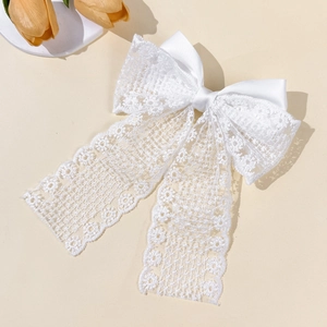 Detail of white lace bow hair clip with floral embroidery and satin center knot