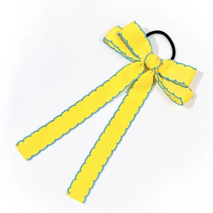 Detail view of yellow bow hair tie with blue scalloped edge and elastic band