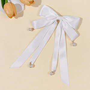 Close-up of a white satin bow hair clip with elegant pearls and long flowing ribbons