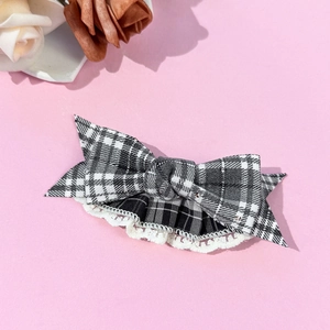 Detail of checkered bow hair clip with lace trim on a soft pink background with dried flowers