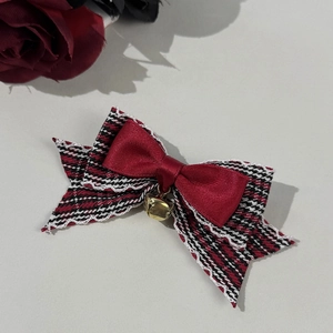 Detail of red satin bow hair clip with houndstooth fabric, lace trim and small gold bell