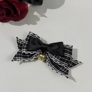 Detail of a plaid bow hair clip with lace edges and a vintage gold metal bell accessory