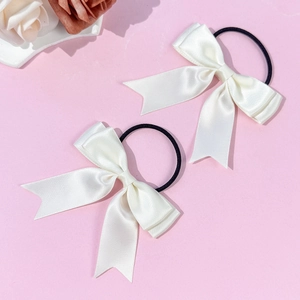 Gros plan détaillé d'une paire de chouchous nœuds en satin blanc sur fond rose pastel