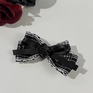 Detail view of plaid tweed bow hair clip with a black ribbon rose and textured fabric