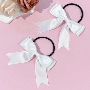 Gros plan d'une paire de nœuds à cheveux en satin blanc avec rubans sur fond rose