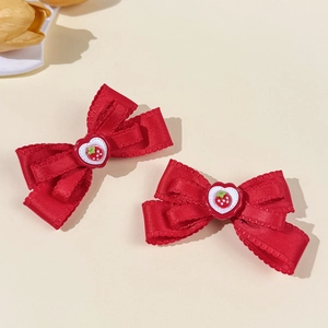 Détail de barrettes nœuds en soie rouge avec breloques fraise cœur et bords en dentelle