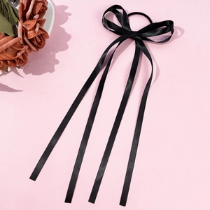 Dettaglio dell'elastico per capelli in raso nero con nastri lunghi su sfondo rosa