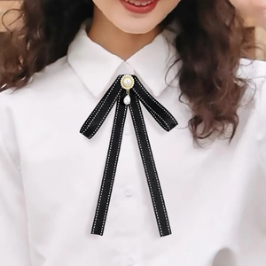 Detail of black ribbon bow brooch with pearl pendant on white shirt collar