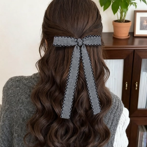 Elegant grey bow hair clip with black stitching on model with long curly hair