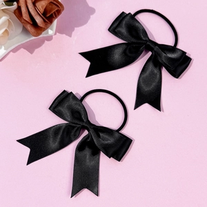 Détail de deux chouchous nœuds en satin noir avec de longs rubans sur fond rose