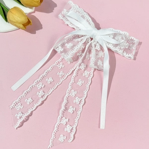 Detailed close-up of elegant white floral lace bow hair clip with flowing satin ribbons