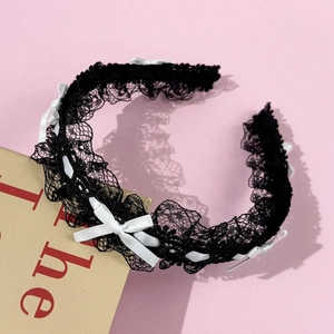 Détail d'un serre-tête en dentelle noire avec petits nœuds blancs sur fond rose