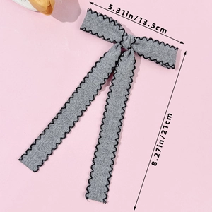 Detail view of a long grey bow hair clip with black zigzag edges and size dimensions