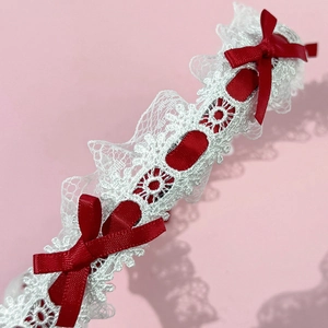 Détail de serre-tête en dentelle blanche orné de petits nœuds en ruban de satin rouge