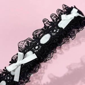 Détail d'un serre-tête en dentelle noire avec des nœuds en satin blanc et bords ondulés
