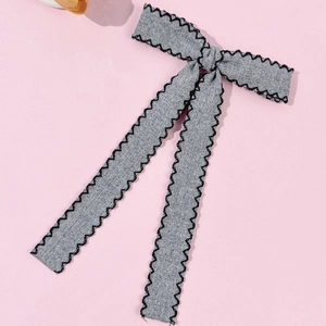 Detailed view of gray fabric bow hair clip with black zigzag stitching and soft streamers