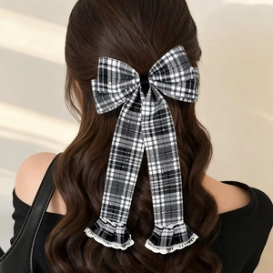 Detail of a black and white plaid bow hair clip with long lace ribbons on wavy hair