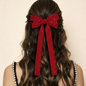 Detail of red velvet bow hair clip with rhinestones on long wavy brown hair