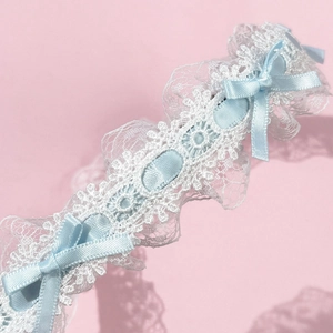 Détail d'un serre-tête en dentelle blanche avec nœuds en ruban bleu sur fond rose