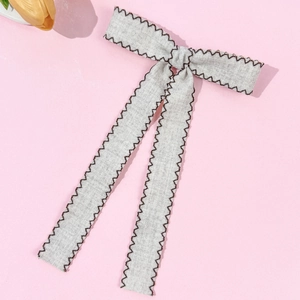Detail of grey bow hair clip with dark brown wavy edges and long elegant ribbons