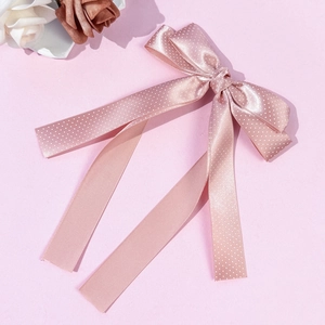 Detail of pink satin bow hair clip with white polka dots and long ribbons on pastel background