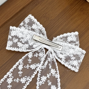 Back view of elegant white lace bow hair clip with silver metal clip on wooden background