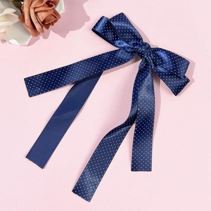 Close-up of navy blue polka dot bow hair clip with ribbons on pink surface