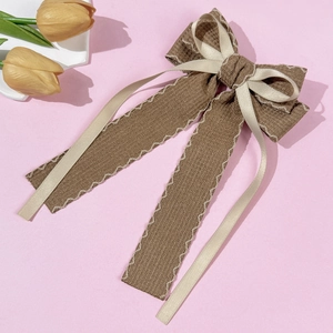 Detail of elegant brown bow hair clip with white wavy stitching and cream ribbon finish
