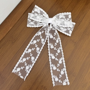 Detail of white floral lace bow hair clip with elegant long ribbons on wooden surface