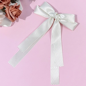 Close-up of elegant white satin bow hair clip with black polka dots and long ribbons